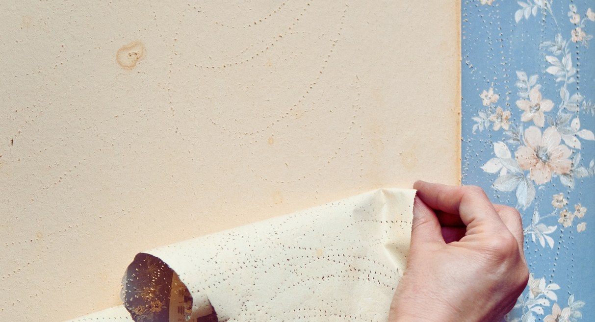 Main décollant un ancien papier peint fleuri sur un mur