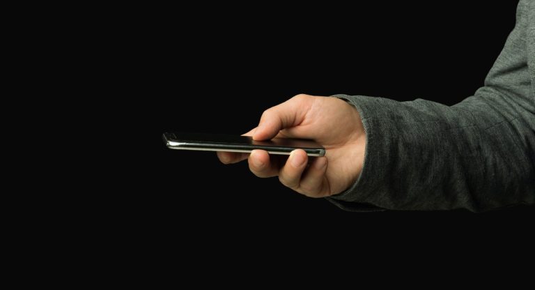 Main tenant un smartphone allumé dans l'obscurité le soir